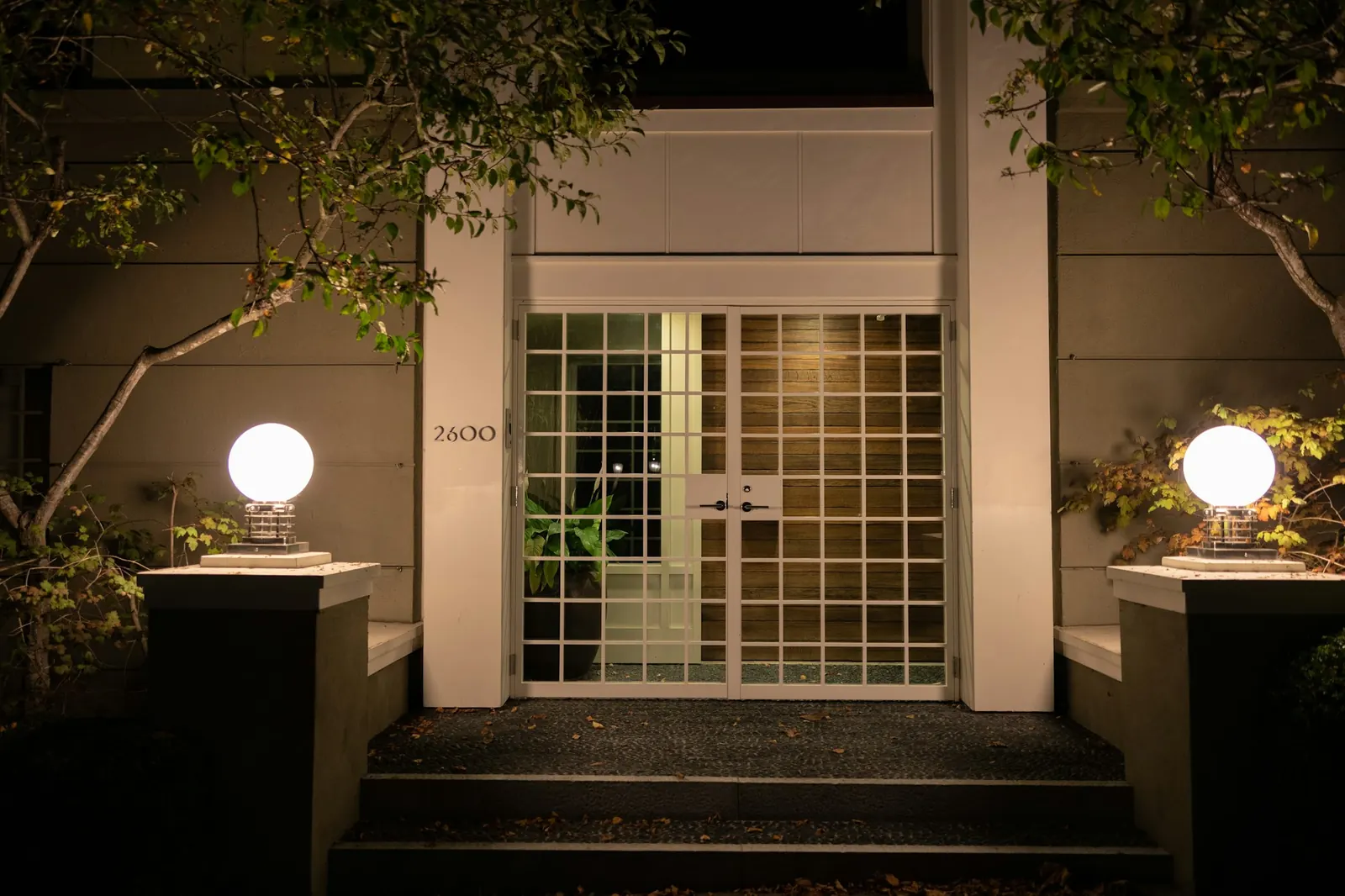 Entrada principal con puertas de vidrio y lámparas de globo cálidas de noche